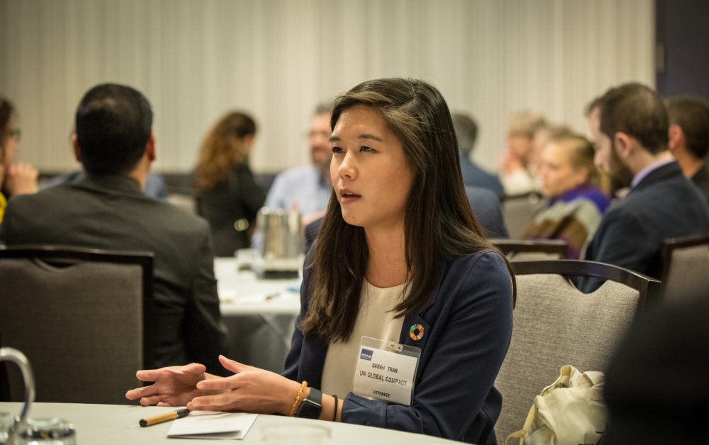 A woman with an Attendee badge sits at a table at the Responsible Business Summit