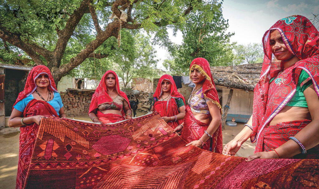 Five women hold up a hand-crafted rug