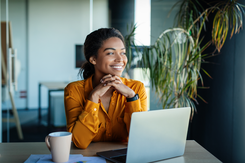 Black woman entrepreneur sitting in front of laptop smiling